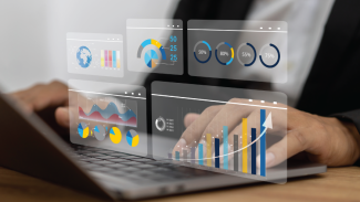 Photo of a hand on a computer with blue and yellow bar charts showing generic data. 