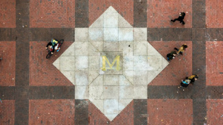 Photo of the famous block M in the middle of the University of Michigan diag with people walking around it. 