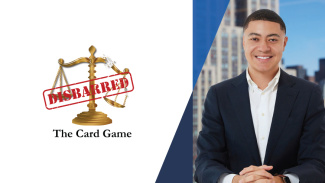 A man in a suit smiles with buildings and a blue sky in the backrgound. To his left, the logo for his card game, Disbarred, is displayed, which is text displayed over a scale.