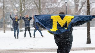 A person holds the Michigan flag out in the snow on the Diag