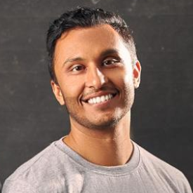 Sulav smiles, wearing a gray shirt and posing in front of a dark gray background