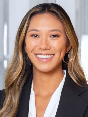 A woman with long brown and blonde hair smiles, wearing a black blazer and white dress shirt in a photo taken inside Ross