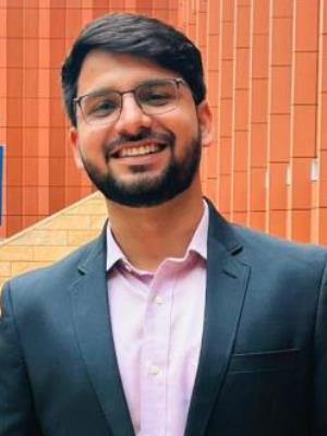 Utkarsh Parashar poses in a blue suit in front of the Ross Winter Garden